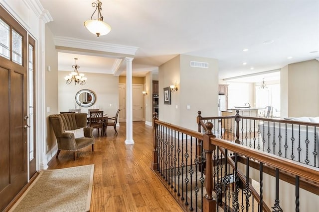 foyer entrance with ornamental molding, wood finished floors, visible vents, and a notable chandelier