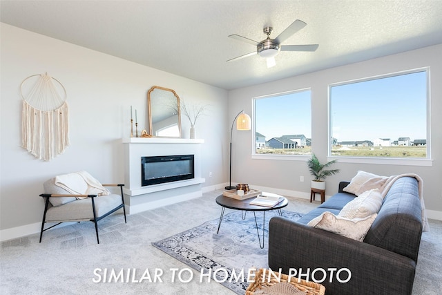 living area with a glass covered fireplace, carpet flooring, baseboards, and ceiling fan