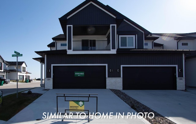 view of front of house with an attached garage, stone siding, a balcony, and concrete driveway