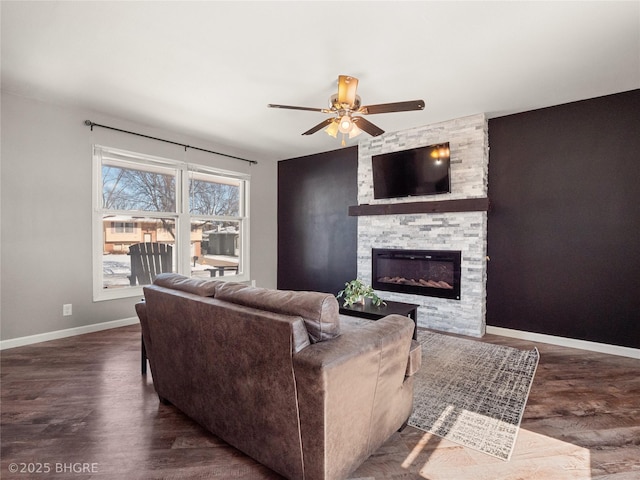 living area featuring dark wood-style floors, a stone fireplace, baseboards, and a ceiling fan