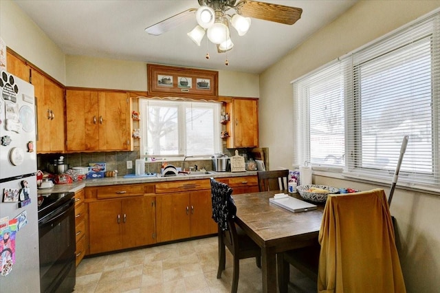 kitchen featuring a sink, light countertops, freestanding refrigerator, black electric range oven, and brown cabinetry