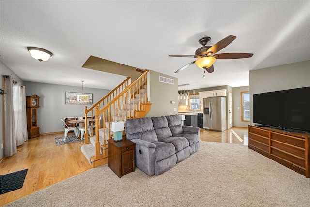 living area featuring light wood finished floors, visible vents, stairway, a ceiling fan, and a textured ceiling