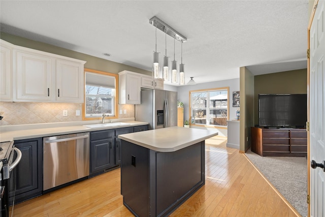 kitchen with a sink, white cabinetry, light countertops, appliances with stainless steel finishes, and decorative light fixtures