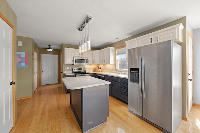 kitchen featuring white cabinets, decorative light fixtures, a center island, stainless steel appliances, and light countertops