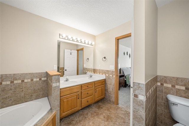 ensuite bathroom with a sink, tile walls, ensuite bath, and a textured ceiling