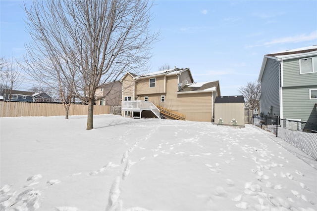 snow covered back of property with stairs, fence, and a deck