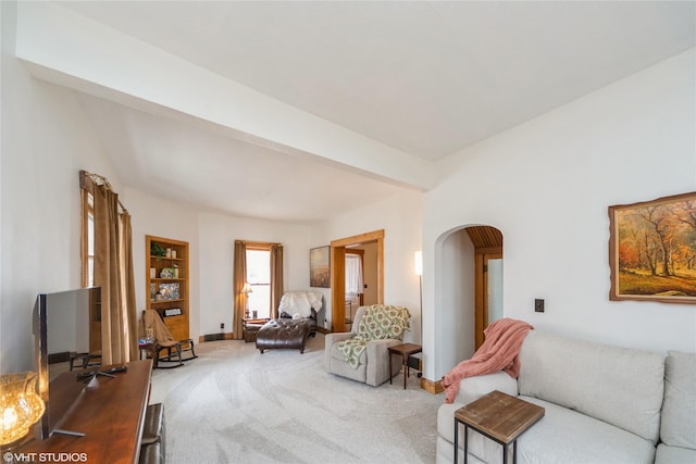 living room featuring arched walkways, carpet floors, beam ceiling, and baseboards