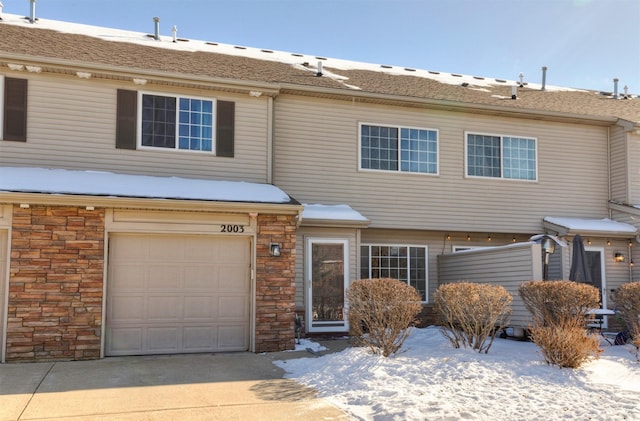 view of property featuring driveway, stone siding, and a garage