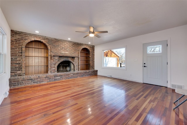 unfurnished living room with built in shelves, a fireplace, visible vents, wood finished floors, and baseboards