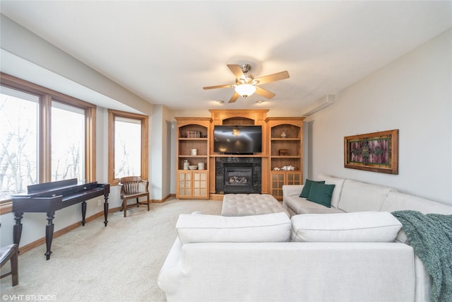 living room featuring a ceiling fan, a glass covered fireplace, light carpet, and baseboards