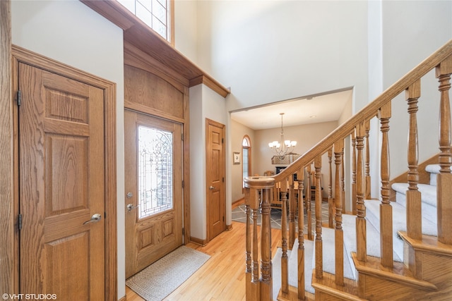 foyer featuring a notable chandelier, a towering ceiling, baseboards, stairs, and light wood-type flooring