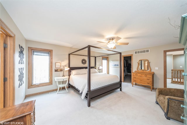 bedroom with light carpet, baseboards, visible vents, a ceiling fan, and a walk in closet