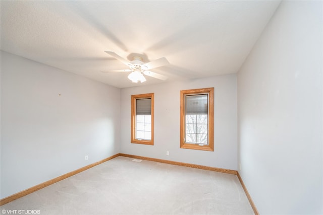 spare room featuring light carpet, ceiling fan, visible vents, and baseboards