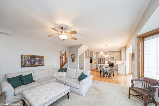 living area featuring light wood-type flooring, ceiling fan, and stairway