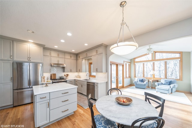 kitchen with under cabinet range hood, gray cabinetry, stainless steel appliances, a sink, and decorative light fixtures