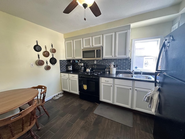 kitchen with dark countertops, dark wood-style flooring, black appliances, white cabinetry, and a sink