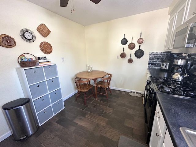 kitchen with dark countertops, stainless steel microwave, backsplash, black gas range oven, and white cabinetry