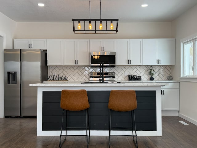 kitchen with white cabinets, a center island with sink, stainless steel appliances, and light countertops