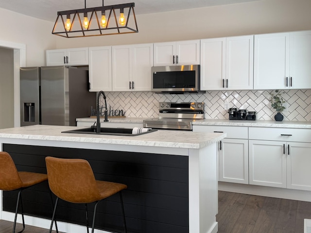 kitchen featuring pendant lighting, a center island with sink, stainless steel appliances, light countertops, and a sink