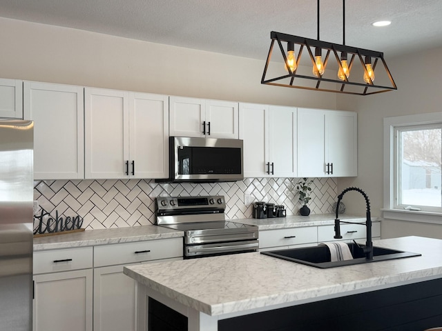 kitchen with pendant lighting, appliances with stainless steel finishes, a kitchen island with sink, white cabinetry, and a sink