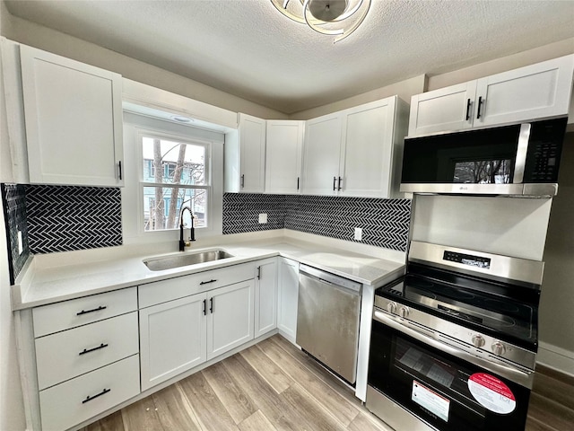 kitchen with stainless steel appliances, a sink, light wood-style floors, white cabinets, and light countertops