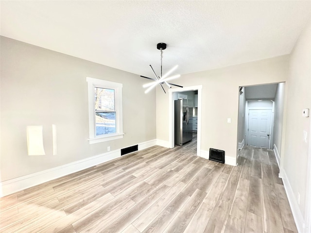 spare room featuring a notable chandelier, light wood-style flooring, baseboards, and a textured ceiling