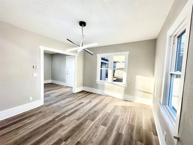 interior space with a notable chandelier, a textured ceiling, baseboards, and wood finished floors