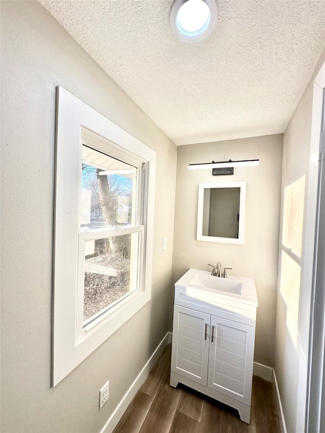 bathroom with a textured ceiling, baseboards, wood finished floors, and vanity