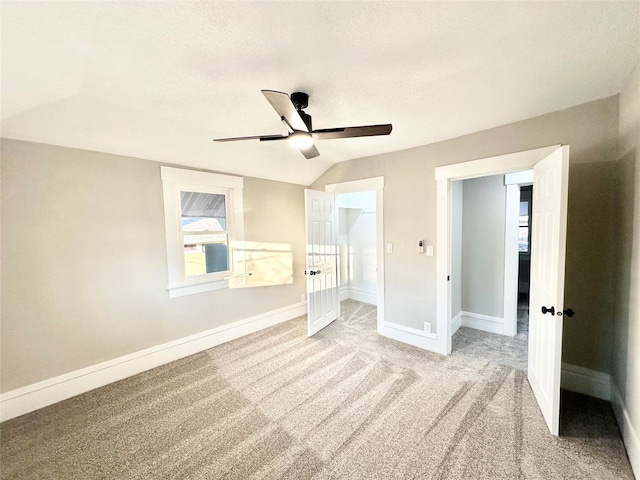 unfurnished bedroom featuring a walk in closet, lofted ceiling, light carpet, a textured ceiling, and baseboards