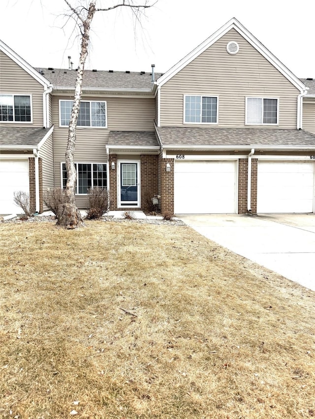 townhome / multi-family property featuring concrete driveway, brick siding, an attached garage, and a front lawn