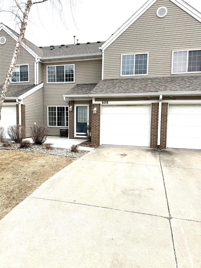 view of front of home with a garage, roof with shingles, concrete driveway, and brick siding