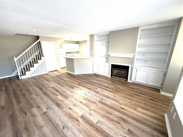 unfurnished living room with a textured ceiling, wood finished floors, a glass covered fireplace, and stairs