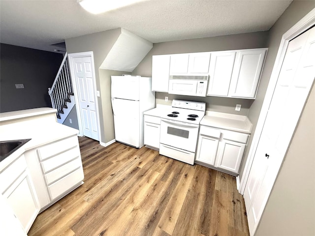 kitchen with a textured ceiling, white appliances, white cabinets, light countertops, and light wood finished floors