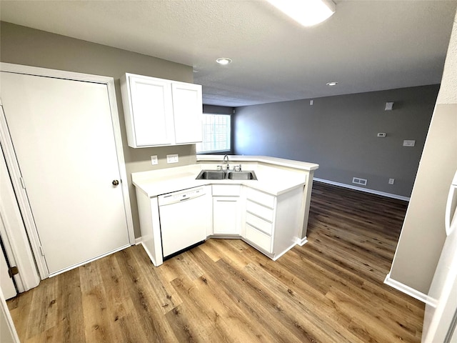 kitchen with light countertops, white cabinets, white dishwasher, a sink, and a peninsula