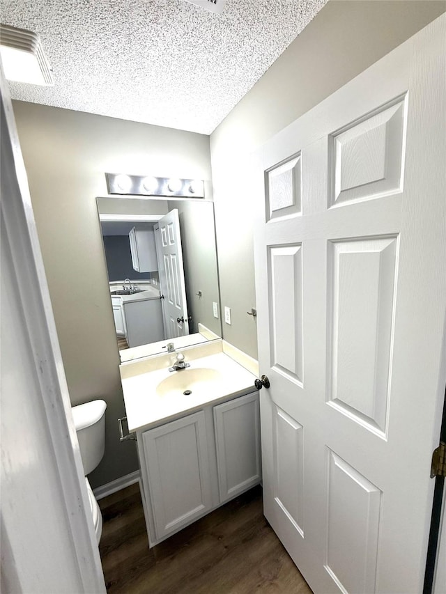 bathroom featuring a textured ceiling, toilet, wood finished floors, vanity, and visible vents