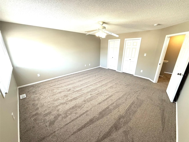 unfurnished bedroom featuring baseboards, visible vents, a textured ceiling, carpet flooring, and multiple closets