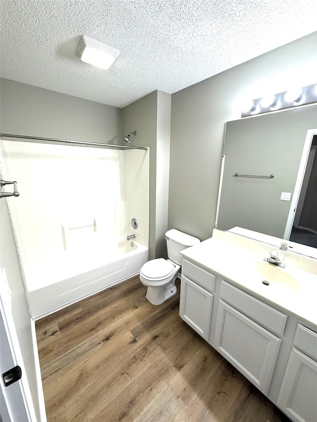 bathroom featuring a textured ceiling, toilet, wood finished floors, vanity, and  shower combination