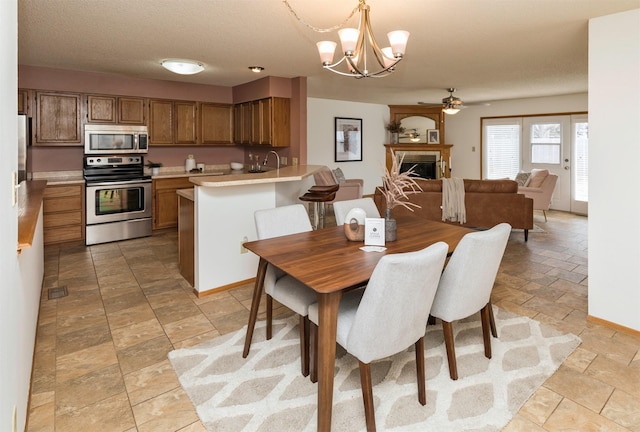 dining space featuring baseboards, ceiling fan with notable chandelier, stone finish floor, and a glass covered fireplace