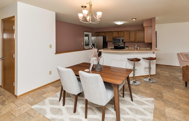 dining area featuring stone finish floor, a notable chandelier, and baseboards