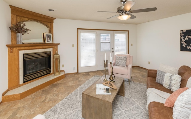 living area with stone finish floor, a tile fireplace, a ceiling fan, and baseboards