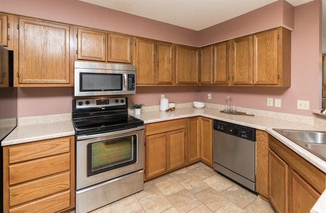 kitchen featuring brown cabinets, appliances with stainless steel finishes, light countertops, and a sink