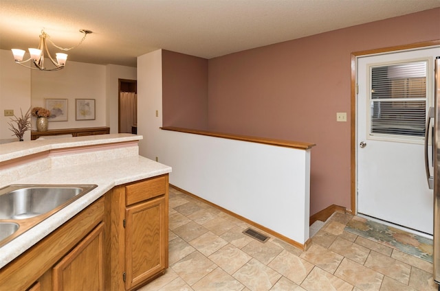 kitchen with visible vents, brown cabinetry, hanging light fixtures, an inviting chandelier, and light countertops