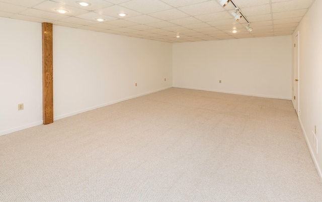 finished basement with baseboards, light colored carpet, a paneled ceiling, and track lighting