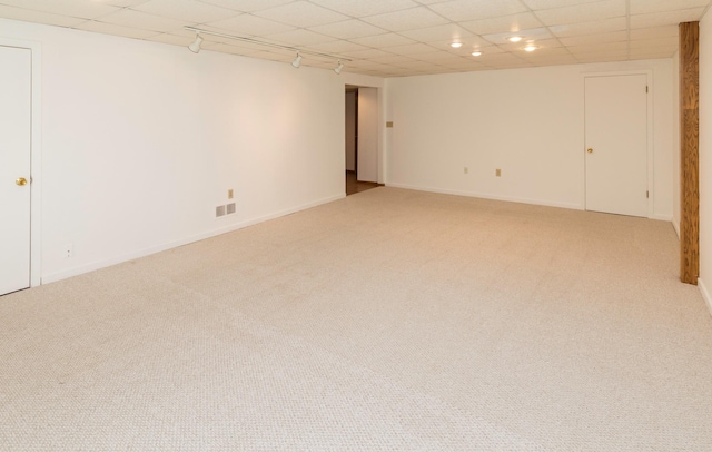 finished below grade area featuring light carpet, baseboards, a paneled ceiling, and track lighting