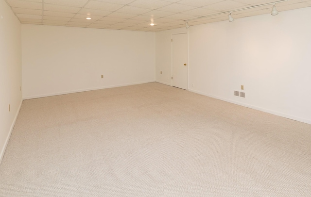 empty room featuring light carpet, visible vents, rail lighting, and baseboards