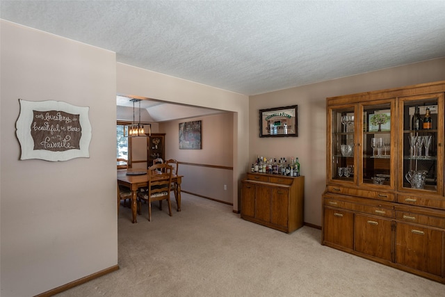 dining area featuring light colored carpet, a notable chandelier, a textured ceiling, and baseboards