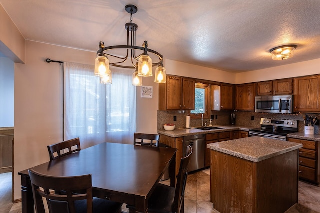 kitchen featuring stainless steel appliances, a sink, a kitchen island, brown cabinets, and pendant lighting