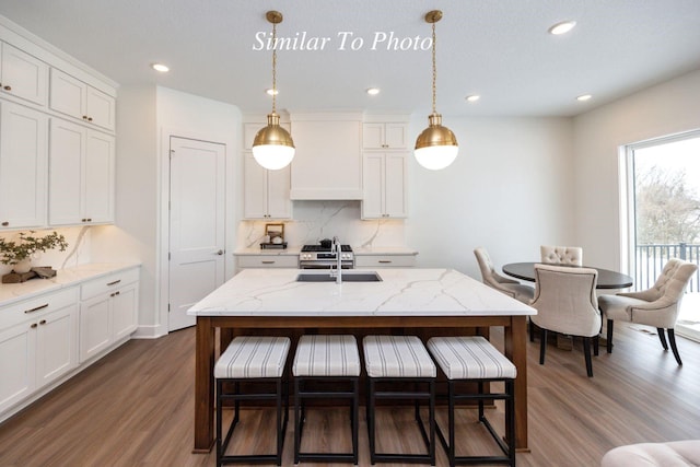 kitchen featuring hanging light fixtures, wall chimney range hood, white cabinetry, and a sink