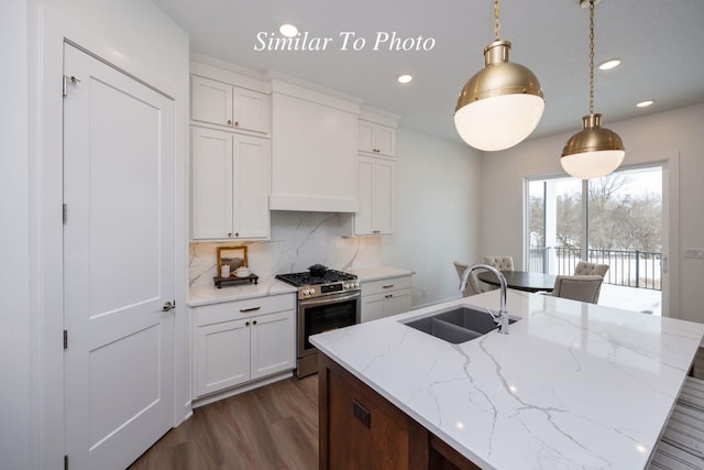 kitchen featuring stainless steel gas range oven, a sink, white cabinets, hanging light fixtures, and light stone countertops