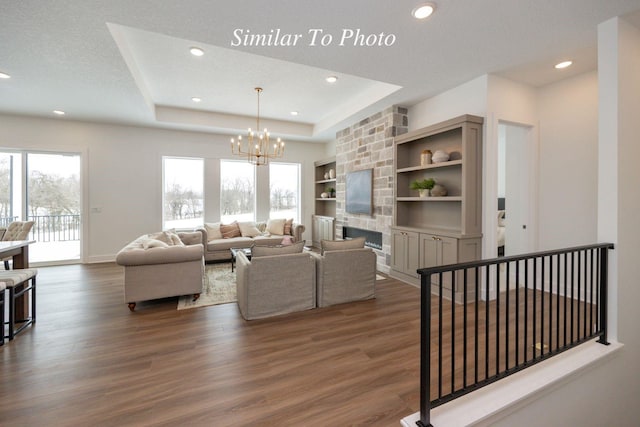 living area featuring a fireplace, a raised ceiling, dark wood finished floors, and an inviting chandelier